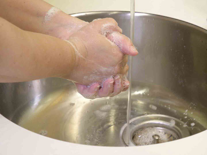 A photo of two hands washing with sopa under running water.